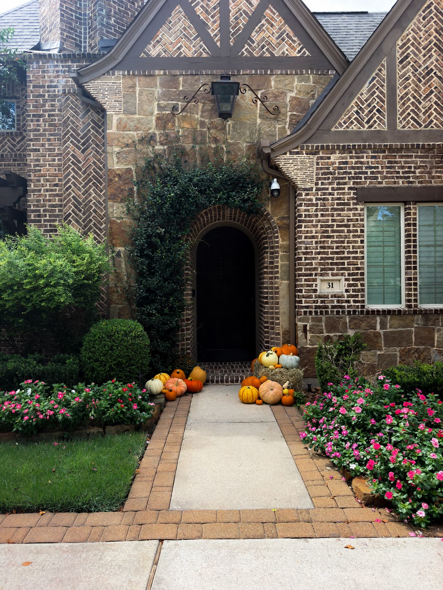 The Porch Edit installed at a brick and stone home in Creekside, Tomball: heirloom pumpkins, hay bale and mums framing an arched front door